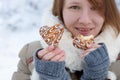 Young woman in winter coat and knitted grey mittens hold beautiful heart shaped biscuit cookies, one bitten, with white icing Royalty Free Stock Photo