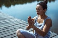 A young woman on a wooden pier sits in a lotus position with her hands folded in a prayer position. Meditation, yoga in nature Royalty Free Stock Photo