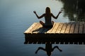 Young woman on wooden pontoon or pier practicing yoga & relaxing with reflection in water .on holiday