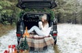 A young woman in a wool hat is sitting in the trunk of a car and holding a Cup of hot tea. The girl smiles. Winter trip Royalty Free Stock Photo