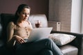 Young woman work at home or stydy on her laptop, holding cup of coffee or tee. Freelance concept. Female sit on leather