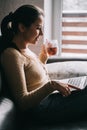 Young woman work at home or stydy on her laptop, holding cup of coffee or tee. Freelance concept. Female sit on leather