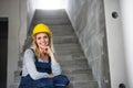 Young woman worker with a yellow helmet sitting on the stairs on the construction site.