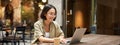 Young woman working in a cafe, using laptop and drinking coffee. Asian girl student with computer studying remotely Royalty Free Stock Photo