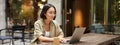 Young woman working in a cafe, using laptop and drinking coffee. Asian girl student with computer studying remotely Royalty Free Stock Photo