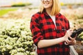 Young woman working in greenhouse. Attractive girl check and count flowers, using tablet computer Royalty Free Stock Photo