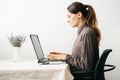 Young woman,working from home during virus quarantine,on her laptop.girl is sitting at white table,in minimalistic interior.cosy Royalty Free Stock Photo