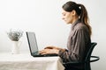 Young woman,working from home during virus quarantine,on her laptop.girl is sitting at white table,in minimalistic interior.cosy Royalty Free Stock Photo