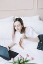 Young woman working on laptop in bed with white linens. Lifestyle composition. Working at home, quarantine concept. Royalty Free Stock Photo