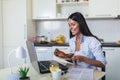 Young woman working with laptop computer and documents while sitting at the kitchen Royalty Free Stock Photo