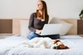 Young woman working on laptop at home, cute small dog sleeping besides. Work from home concept Royalty Free Stock Photo