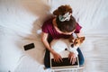 young woman working on laptop at home, sitting on the couch, cute small dog besides. Technology and pets concept Royalty Free Stock Photo