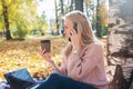 Young woman working with laptop outdoors and holding phone