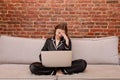 Young woman is working on laptop on sofa at home, holds hand on head, having headache, migraine, sad female freelancer Royalty Free Stock Photo