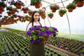 Young woman working in nursery garden and showing pot with beautiful blooming peetunia flower. Growing flowers Royalty Free Stock Photo