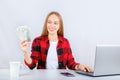 Young woman working online on computer earning money dollar bills banknotes.