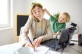 Young woman working online using laptop at home. Home office and parenthood at same time. Exhausted parent with hyperactive child Royalty Free Stock Photo