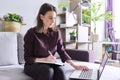 Young woman working remotely at home, sitting on sofa with laptop Royalty Free Stock Photo
