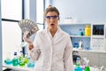 Young woman working at scientist laboratory holding money scared and amazed with open mouth for surprise, disbelief face Royalty Free Stock Photo