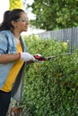 Young woman working on the yard cutting bush with hedge shear while smiling