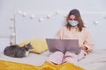 Young woman works in a face mask from home. A girl in quarantine due to coronavirus with a laptop and a pet, home lifestyle