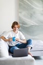 Young woman works on the laptop with cup of coffee on a sofa Royalty Free Stock Photo
