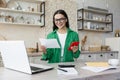 A young woman works and studies at home using a laptop. She is sitting in the kitchen, holding documents in her hands Royalty Free Stock Photo