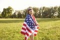 Young woman wrapped in American flag in countryside. Pretty girl with US national banner outdoors. Independence day Royalty Free Stock Photo