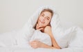 Young woman wrapped in soft blanket sitting on bed. Smiling girl sitting in bed and smiling at home. Royalty Free Stock Photo