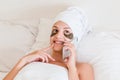 Young woman wrapped in towel after shower and with patches under eyes is relaxing in bed and talking oh her phone. Perfect and Royalty Free Stock Photo