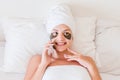 Young woman wrapped in towel after shower and with patches under eyes is relaxing in bed and talking oh her phone. Perfect and Royalty Free Stock Photo