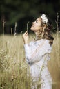 Young woman with a wreath in her head in a white dress in a boho style in the field. Vertical. Unity with nature