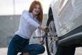 Young woman with wrench changing wheel on a broken car