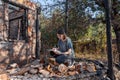 Young woman writes on the papers sitting in front of house destroyed with fire.