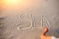 A young woman writes in the sand the word sea