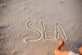 A young woman writes in the sand the word sea