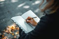 Young woman writing in a diary in an autumn park. Closeup image of a woman writing on a blank notebook. Woman working Royalty Free Stock Photo