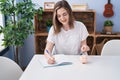 Young woman writing on notebook inserting coin on piggy bank at home Royalty Free Stock Photo