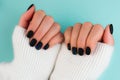 Woman& x27;s hands in white knitted sweater on blue background. Perfect black matte manicure gel polish