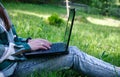 Young woman& x27;s legs on the green grass with open laptop. Girl& x27;s hands on keyboard. Distance learning concept Royalty Free Stock Photo