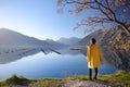 Young woman in yellow coat standing on the coast of Adriatic sea and admiring of stunning winter view of Boka Kotor Bay seascape.