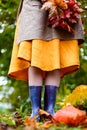 Young woman in yellow dress, cardigan, linen apron, blue rubber boots with bouquet of red maple leaves. Autumn harvest. Cut orange Royalty Free Stock Photo