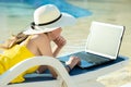 Young woman in yellow dress is laying on beach chair working on computer laptop connected to wireless internet typing text on keys