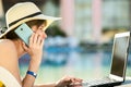 Young woman in yellow dress is laying on beach chair working on computer laptop having conversation on mobile phone in summer Royalty Free Stock Photo