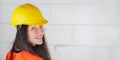 Young woman in yellow hard hat and orange high visibility vest, long dark hair, looking over her shoulder, smiling confident. Royalty Free Stock Photo