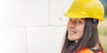 Young woman in yellow hard hat and orange high visibility vest, long dark hair, looking over her shoulder, smiling confident. Royalty Free Stock Photo