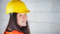 Young woman in yellow hard hat and orange high visibility vest, long dark hair, looking over her shoulder, smiling confident. Royalty Free Stock Photo