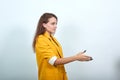 Young woman in yellow jacket doing greeting gesture isolated on gray wall