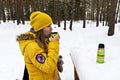 Young woman in a yellow jacket drinking hot tea from a thermos on a hike in a winter snowy forest. Active lifestyle, winter walks Royalty Free Stock Photo