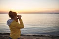 Young woman in a yellow jacket looking through binoculars and enjoying a beautiful view of the coastal landscape Royalty Free Stock Photo